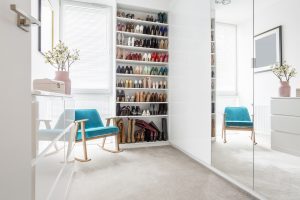 Large shoe wardrobe next to a blue, comfortable chic chair standing in a woman's white room